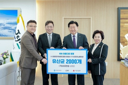 네 사람이 후원 물품 전달 판을 들고 선 기념 사진