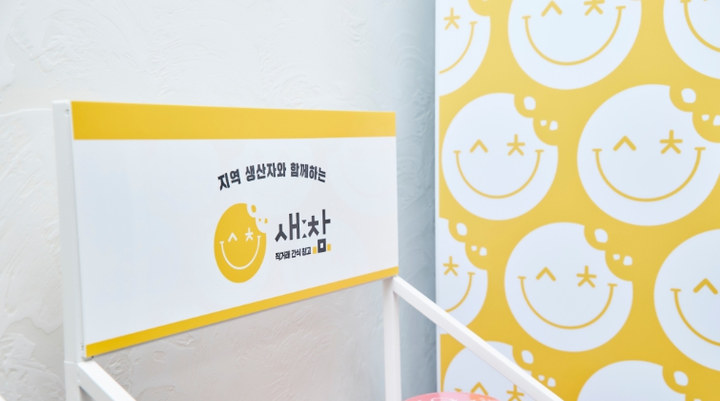 노랑 스마일 얼굴이 반복된 벽면 앞에 선 새참 간판