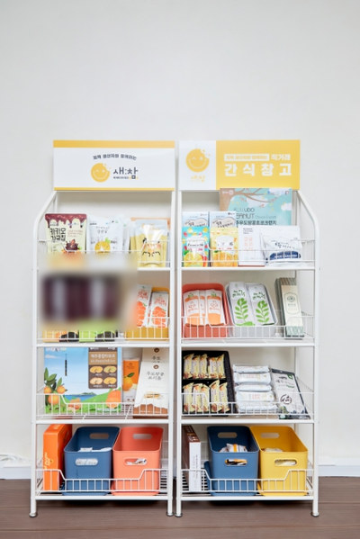 아래 칸에 수납 바구니를 둔 두 칸짜리 흰 철제 간식 선반